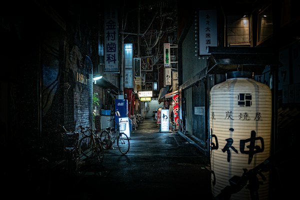 Black bicycle parked beside building during night time — Osaka, Japan