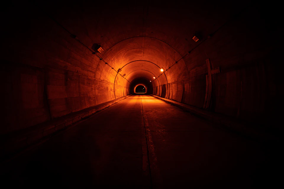 Long road tunnel lit from within, receding toward a distant opening