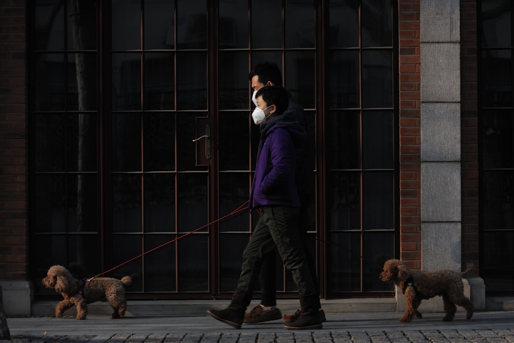 man in black jacket and black pants standing beside brown dog