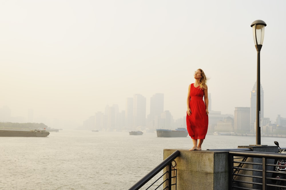 woman in red long sleeve dress standing on gray concrete bridge during daytime
