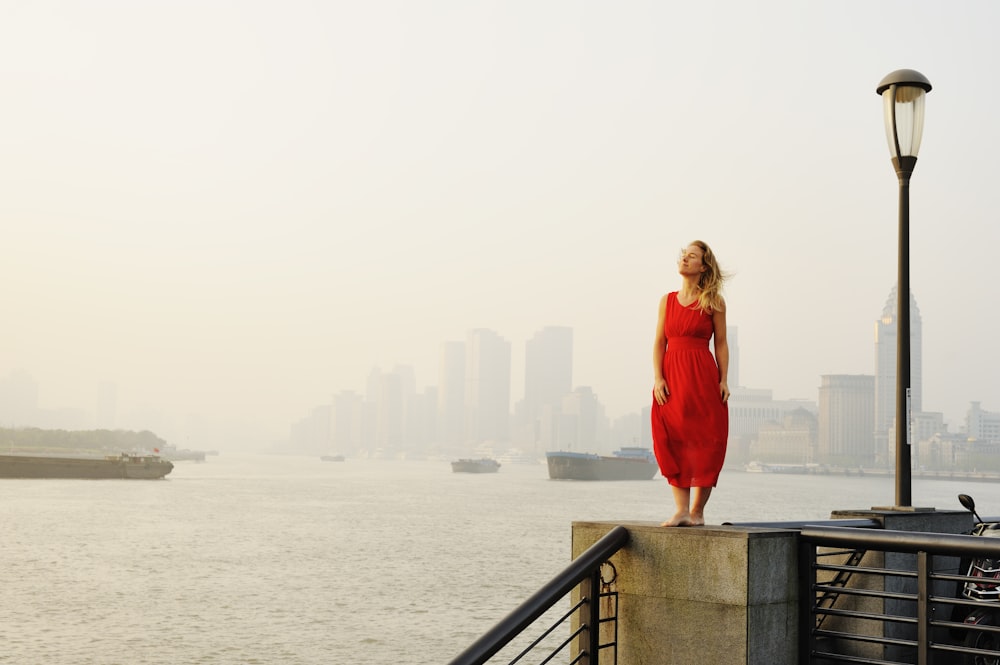 Femme en robe rouge à manches longues debout sur un pont en béton gris pendant la journée