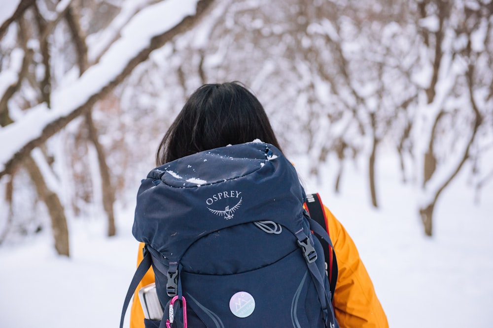 person in black and orange jacket with black backpack standing on snow covered ground during daytime
