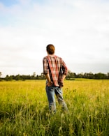 man in red and white plaid dress shirt and blue denim jeans standing on green grass