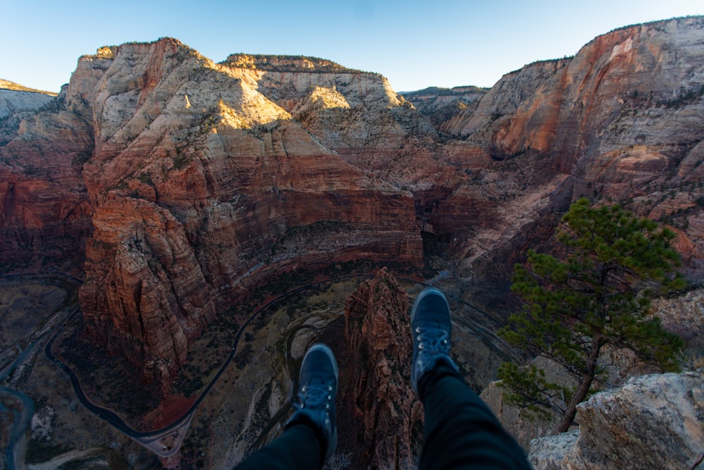 person in blue denim jeans and blue sneakers sitting on cliff during daytime