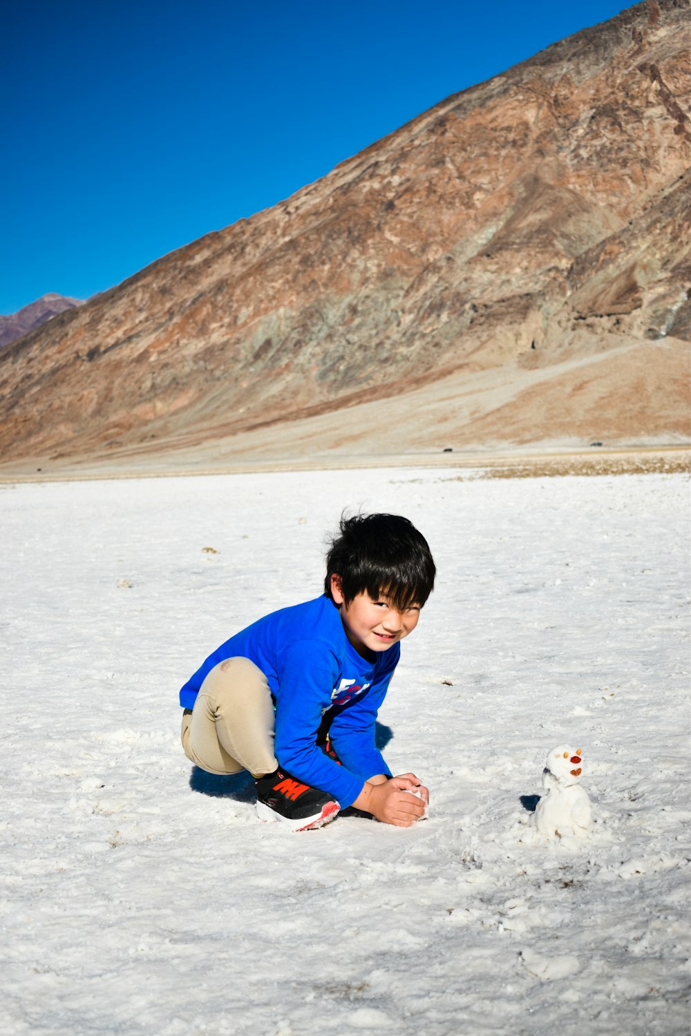 boy in blue and red jacket playing on snow covered ground during daytime