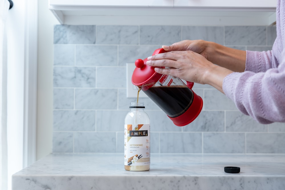 person pouring red liquid on white plastic bottle