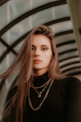 Fashion-forward young woman wearing delicate layered necklaces against an urban mural.