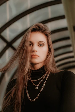 Fashion-forward young woman wearing delicate layered necklaces against an urban mural.