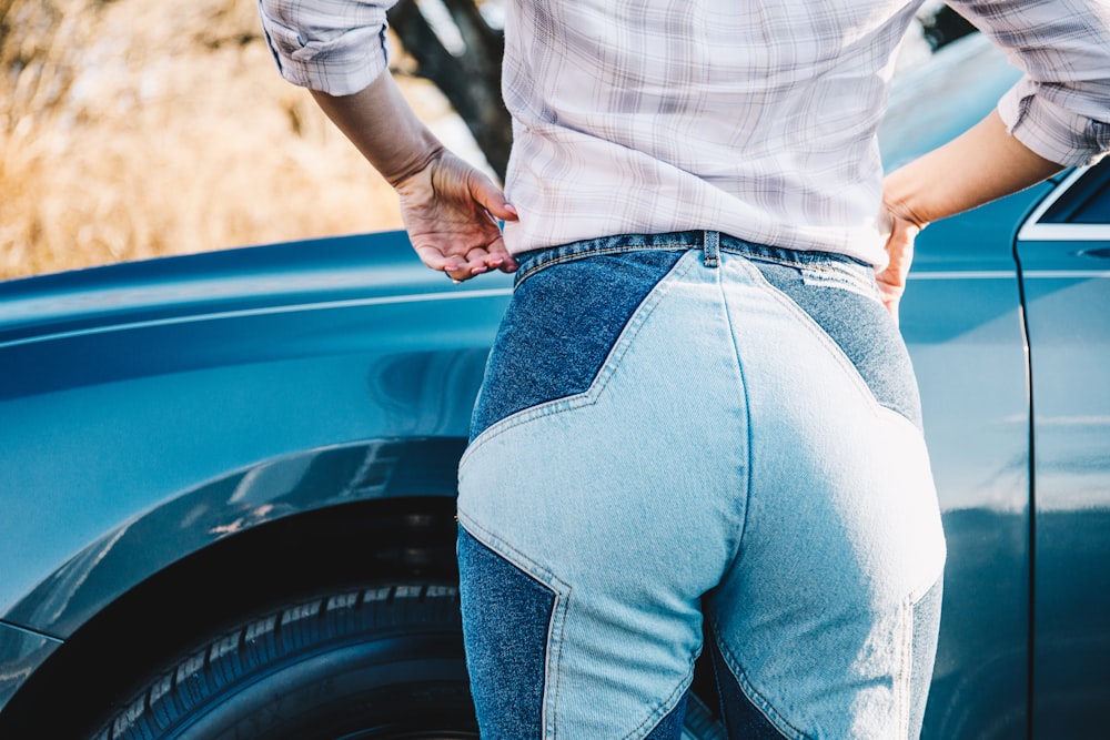 person in white and gray plaid shirt and blue denim jeans sitting on blue car