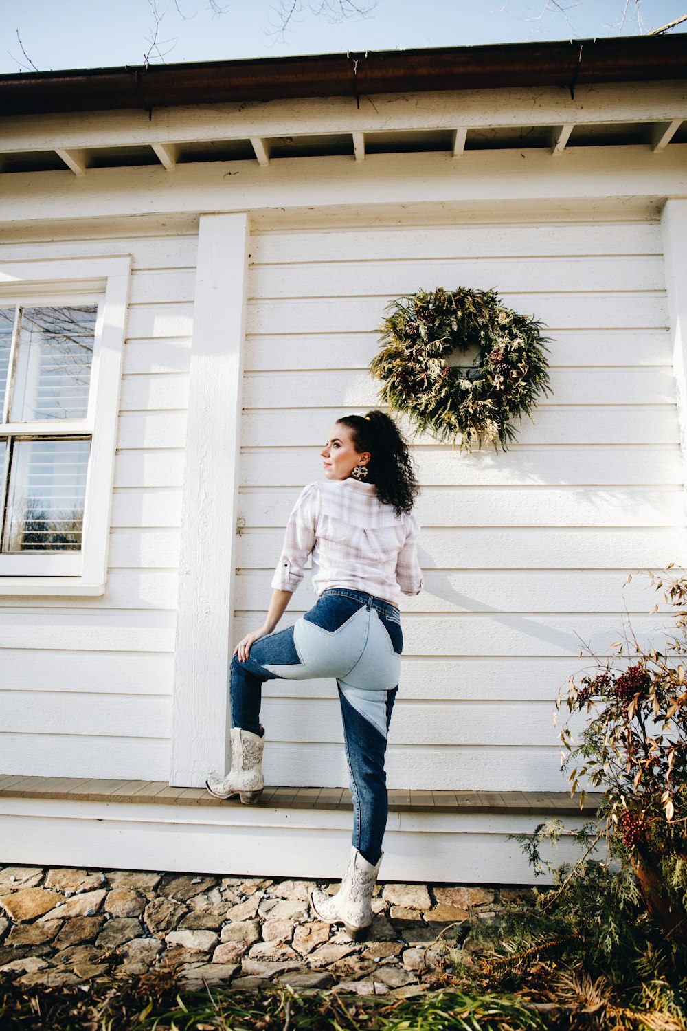 woman in white long sleeve shirt and blue denim jeans standing beside white wooden door