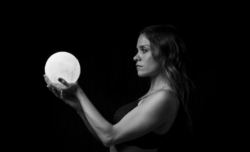 A woman gently holding a glowing silver orb under a midnight blue sky.