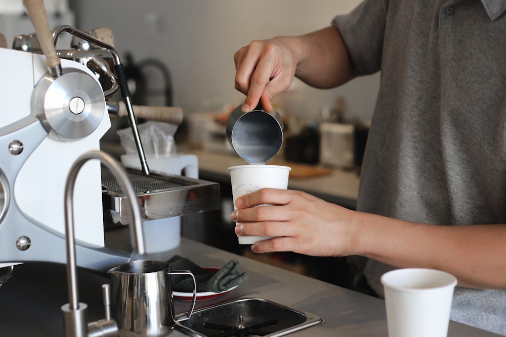 person pouring white liquid on white ceramic mug