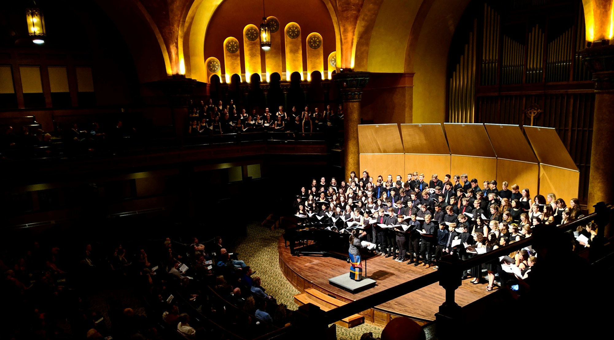 A choir performs for a large audience in a concert hall.