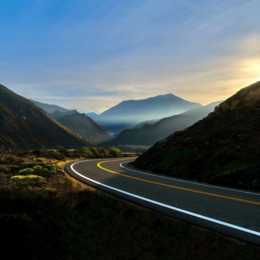 gray concrete road near green mountains during daytime