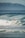 A surfer rides a wave with skill and determination, surrounded by the ocean's powerful waves and framed against a distant mountain range. The scene captures a dynamic moment in the sport of surfing.