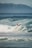 A surfer rides a wave with skill and determination, surrounded by the ocean's powerful waves and framed against a distant mountain range. The scene captures a dynamic moment in the sport of surfing.