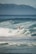 A surfer rides a wave with skill and determination, surrounded by the ocean's powerful waves and framed against a distant mountain range. The scene captures a dynamic moment in the sport of surfing.