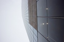 A skyscraper with a grid of reflective glass panels stretching upwards into a cloudy sky, creating a sense of height and modernity.