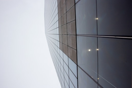 A skyscraper with a grid of reflective glass panels stretching upwards into a cloudy sky, creating a sense of height and modernity.