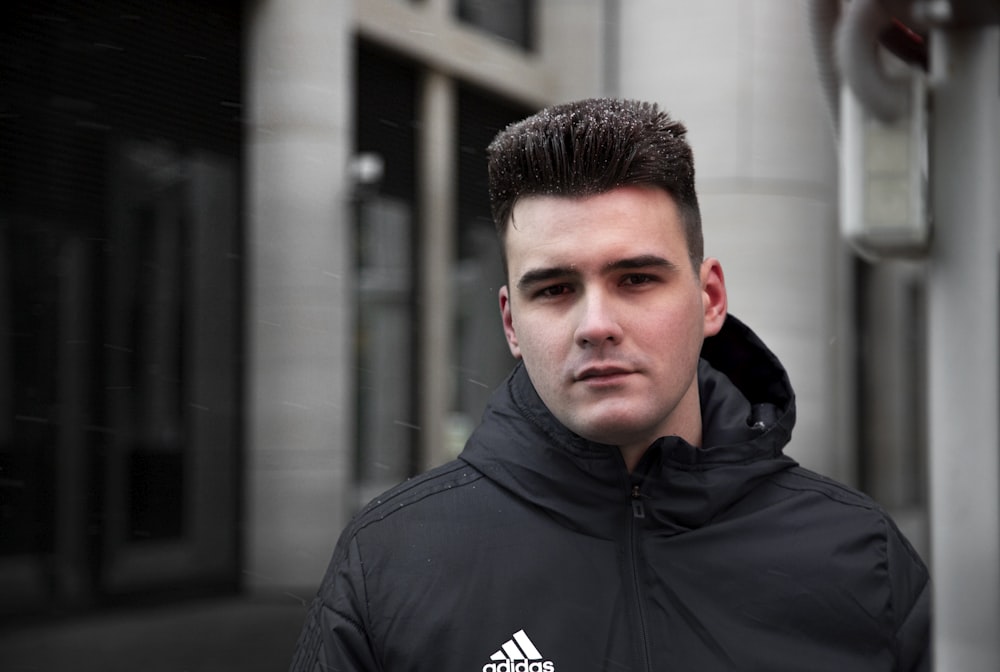 man in black and white adidas hoodie standing near building during daytime