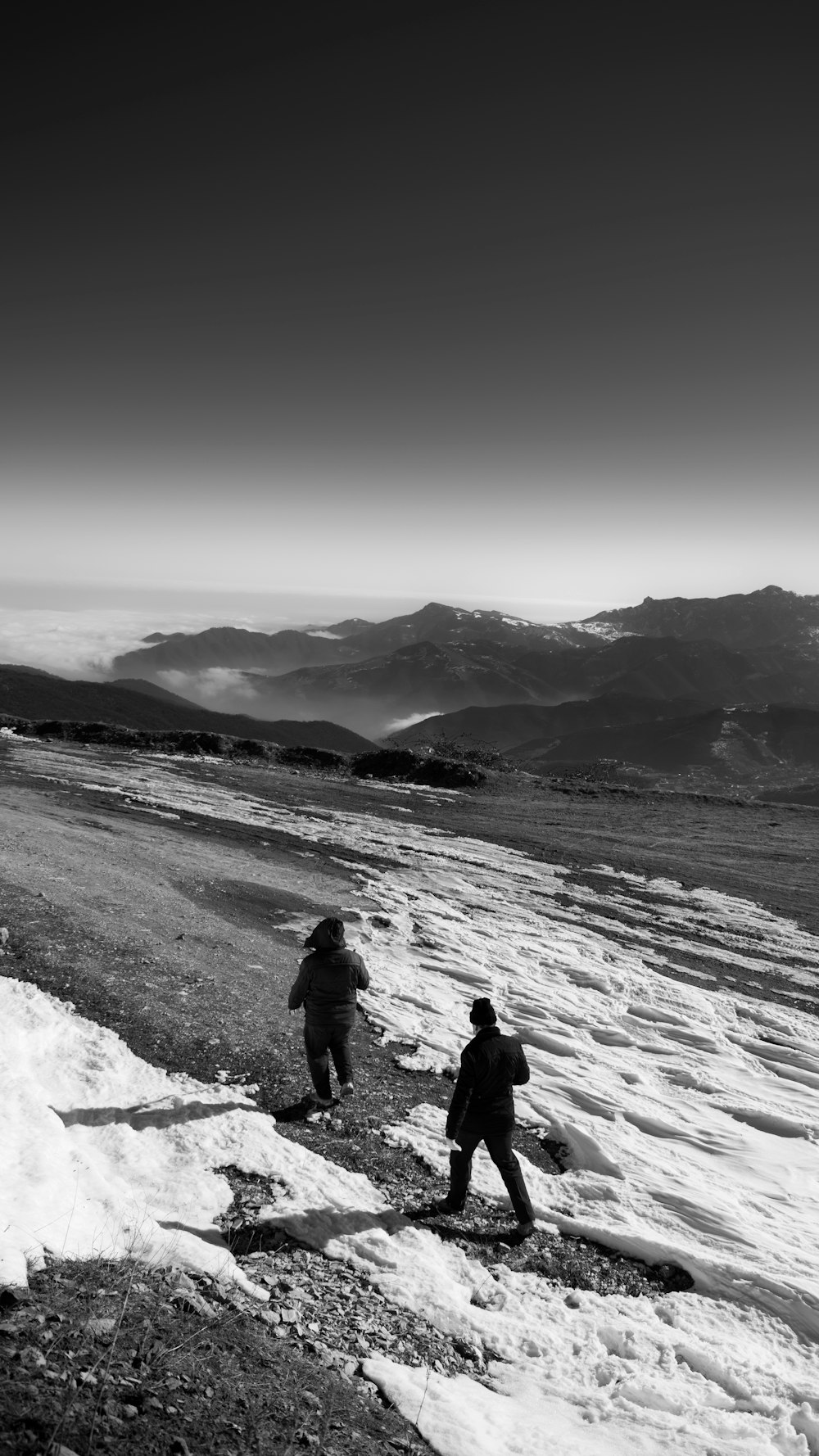 grayscale photo of 2 person walking on snow covered ground