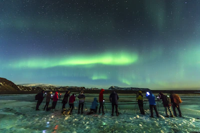 Personas observando y videograbando auroras boreales en Islandia.