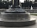 A monument with engravings featuring emblems of the Navy and Army Air Forces, including an inscription that reads 'AMERICANS CAME TO LIBERATE'. The setting appears to be an outdoor memorial area with stone structures and a visible fountain in the background.