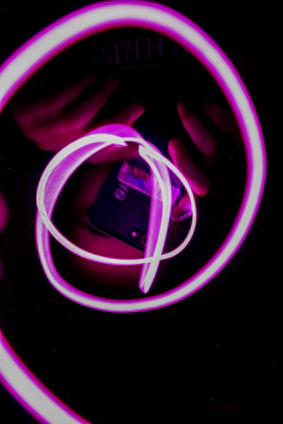A sleek dark interface glowing with neon pink accents and floating pink particles around a rotating cassette icon.