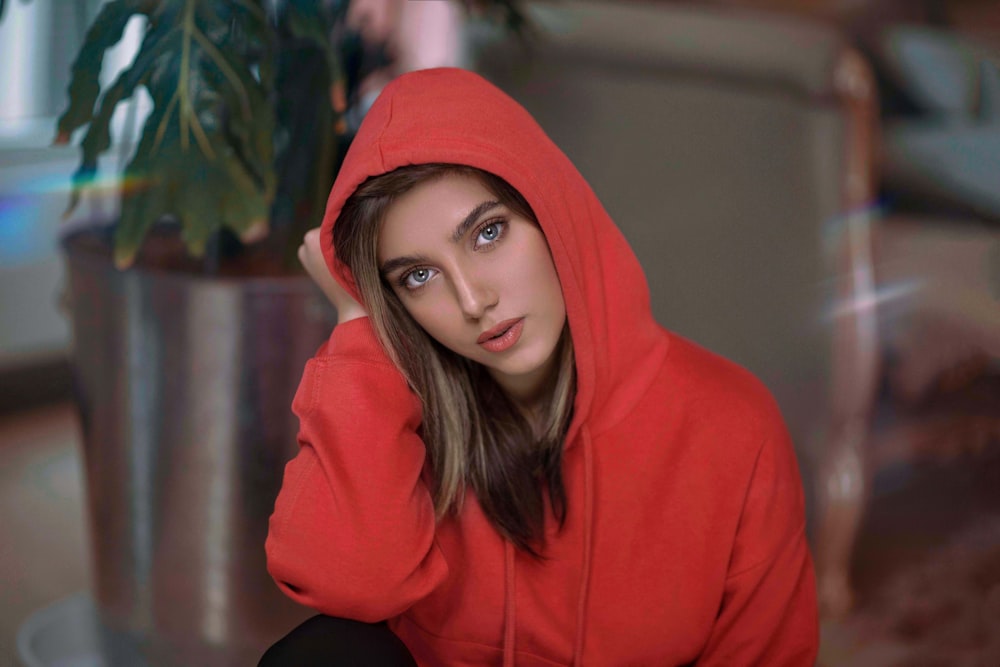 femme en sweat à capuche rouge debout près de la plante verte