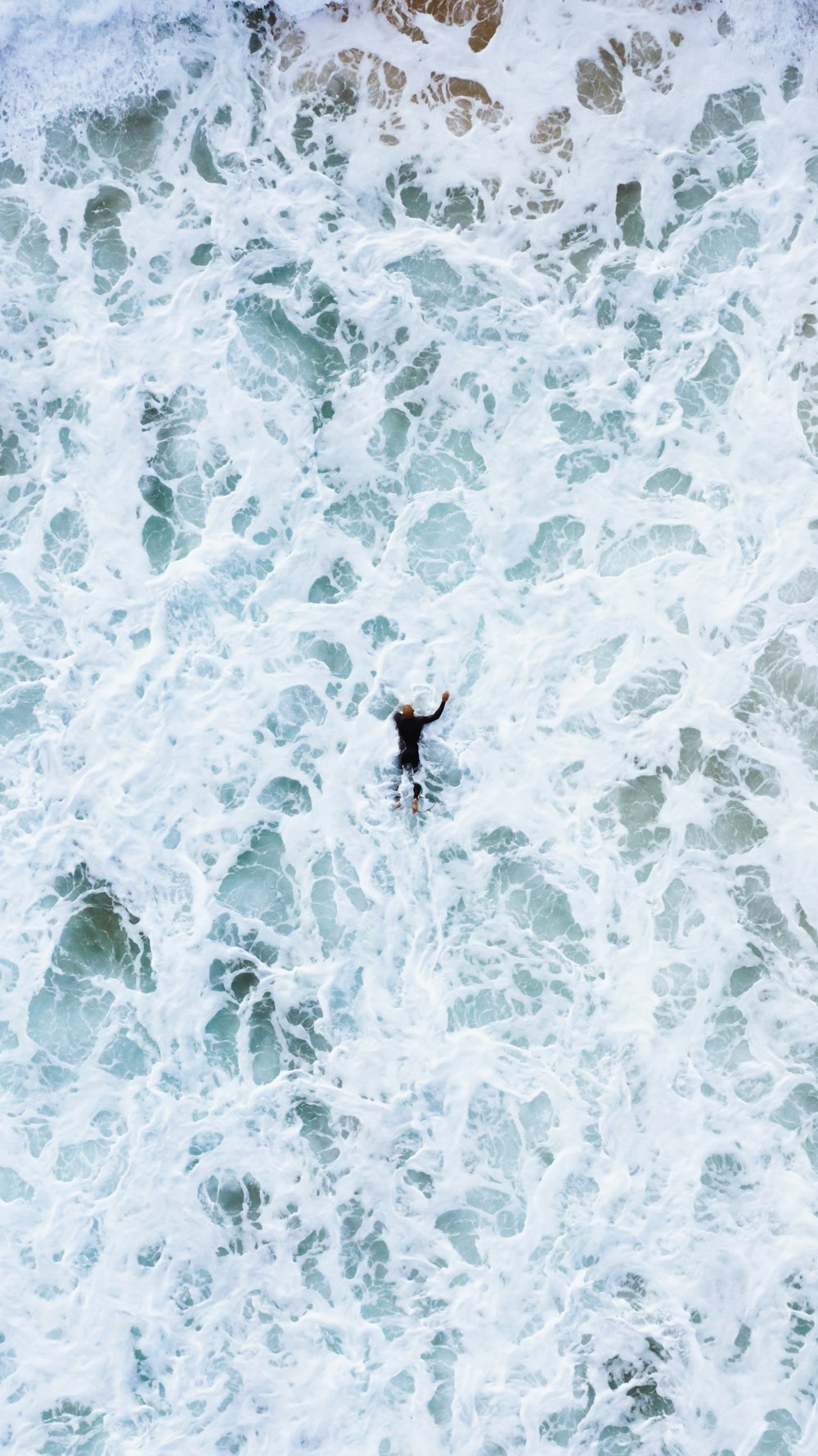 Person in schwarzen Shorts und schwarzem Hemd auf blauem und weißem Wasser stehend