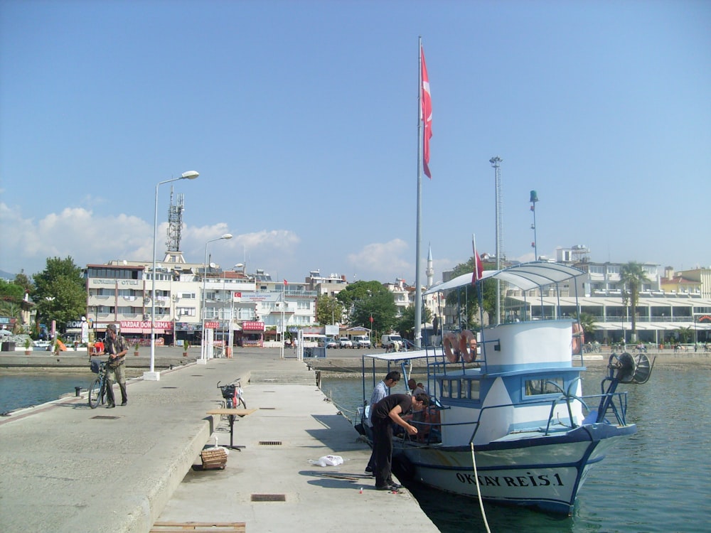 people walking on sidewalk near white and blue boat during daytime