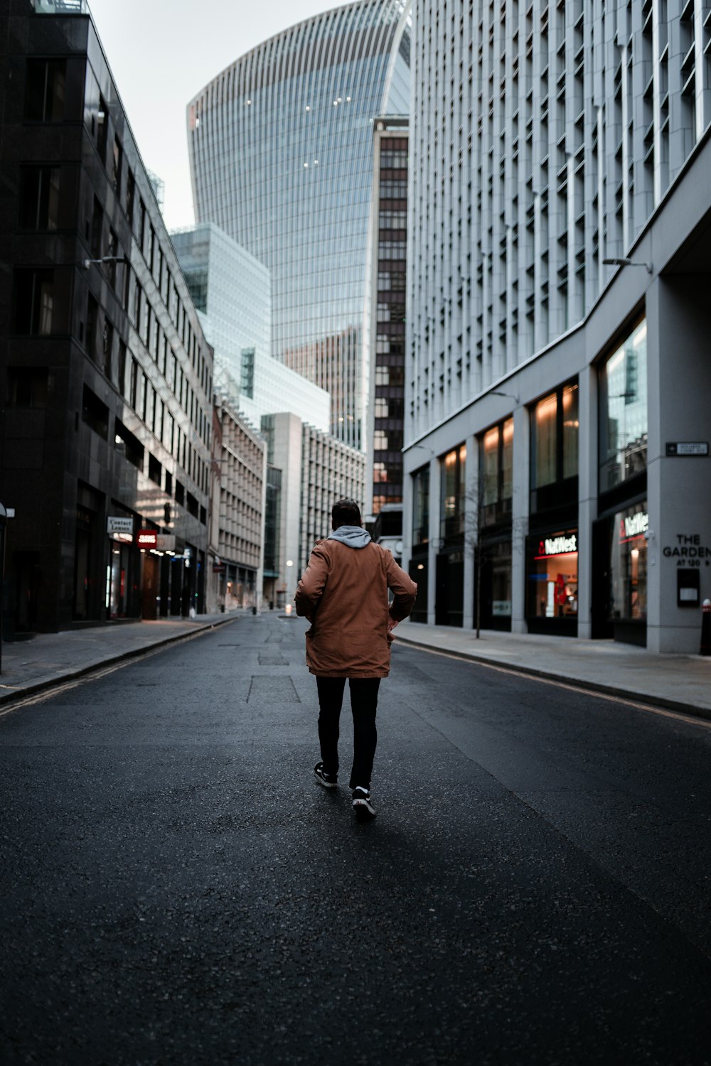 Hombre en chaqueta marrón caminando en la acera durante el día