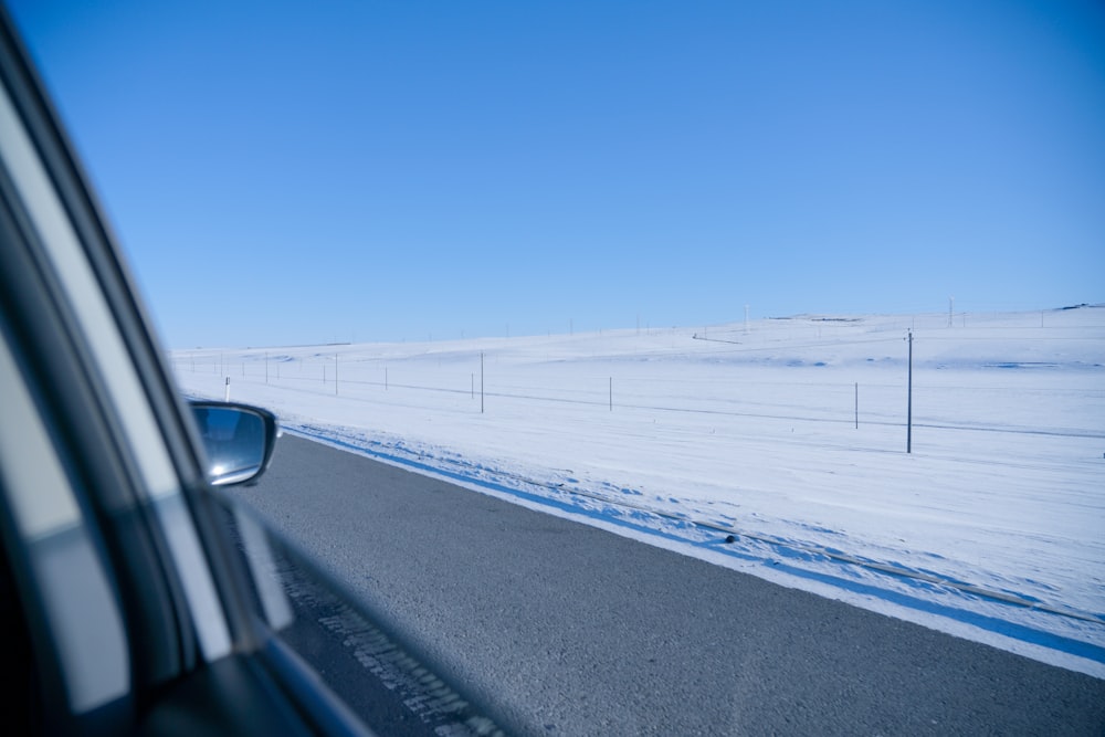 black asphalt road between snow covered field under blue sky during daytime
