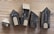 A series of five small, handcrafted wooden houses with black bodies and beige roofs, placed on a wooden surface. Each house is decorated with simple white window and door designs, giving a quaint village-like appearance.