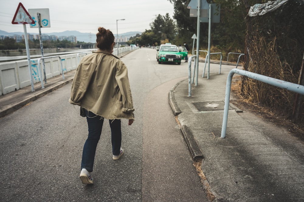 woman in brown coat and blue denim jeans standing on gray asphalt road during daytime