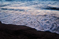 Close-up of delicate waves gently breaking on a dark sandy beach at twilight.