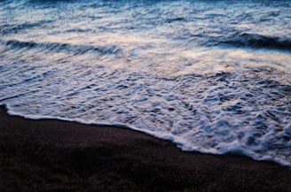 Close-up of delicate waves gently breaking on a dark sandy beach at twilight.
