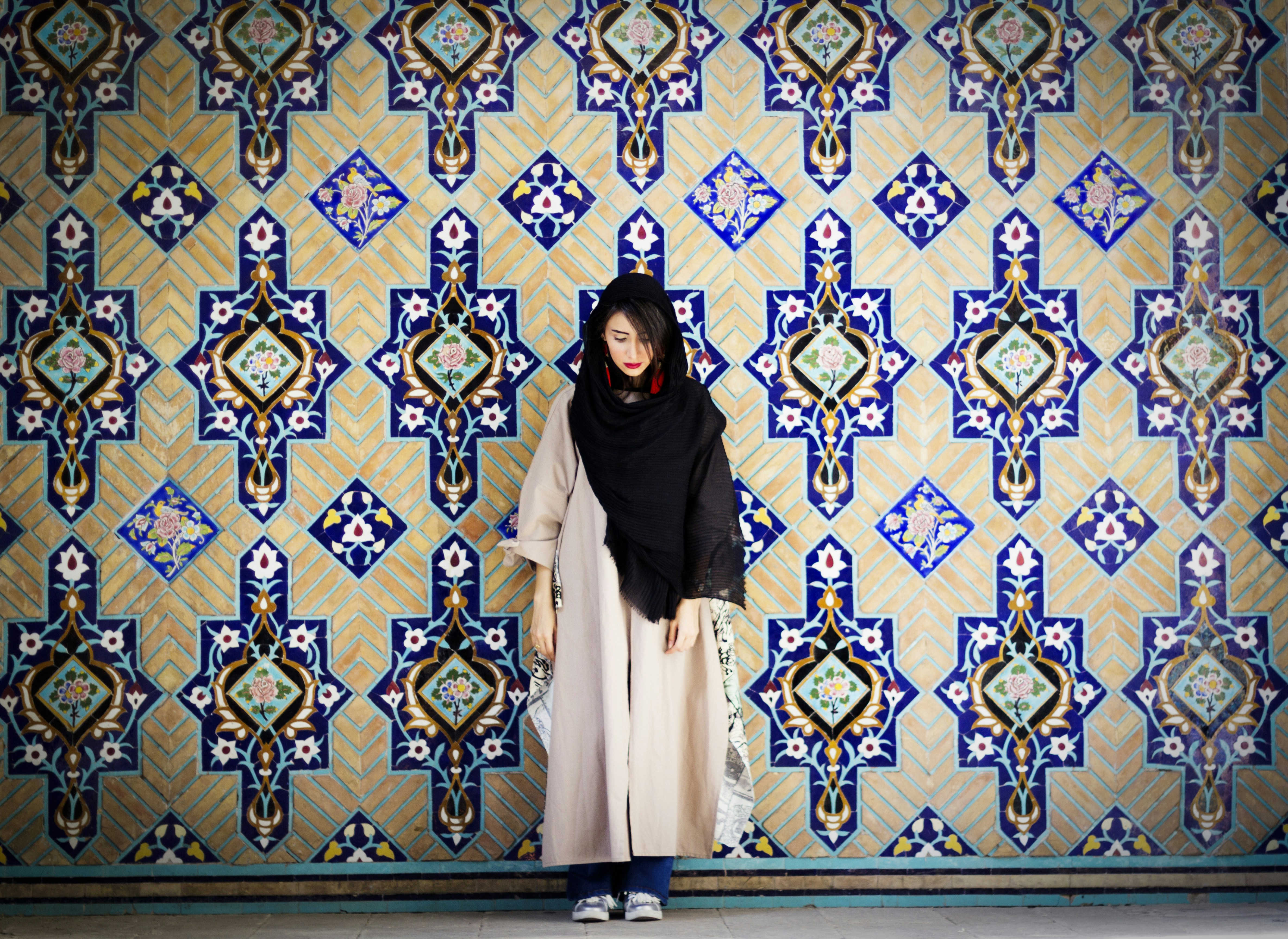 wanita berhijab hitam berdiri di atas karpet bunga biru dan kuning