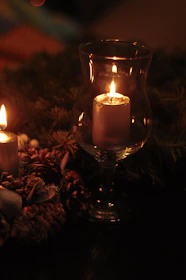 A cozy scene showing a lit candle surrounded by greenery and soft white linens.