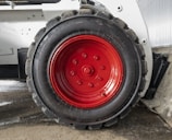 A close-up view of a large, rugged tire with a bright red hubcap mounted on a heavy-duty vehicle. The tire sidewall shows the brand name 'GALAXY' embossed on it. The surrounding area includes parts of the vehicle’s white frame and a concrete floor.