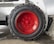 A close-up view of a large, rugged tire with a bright red hubcap mounted on a heavy-duty vehicle. The tire sidewall shows the brand name 'GALAXY' embossed on it. The surrounding area includes parts of the vehicle’s white frame and a concrete floor.