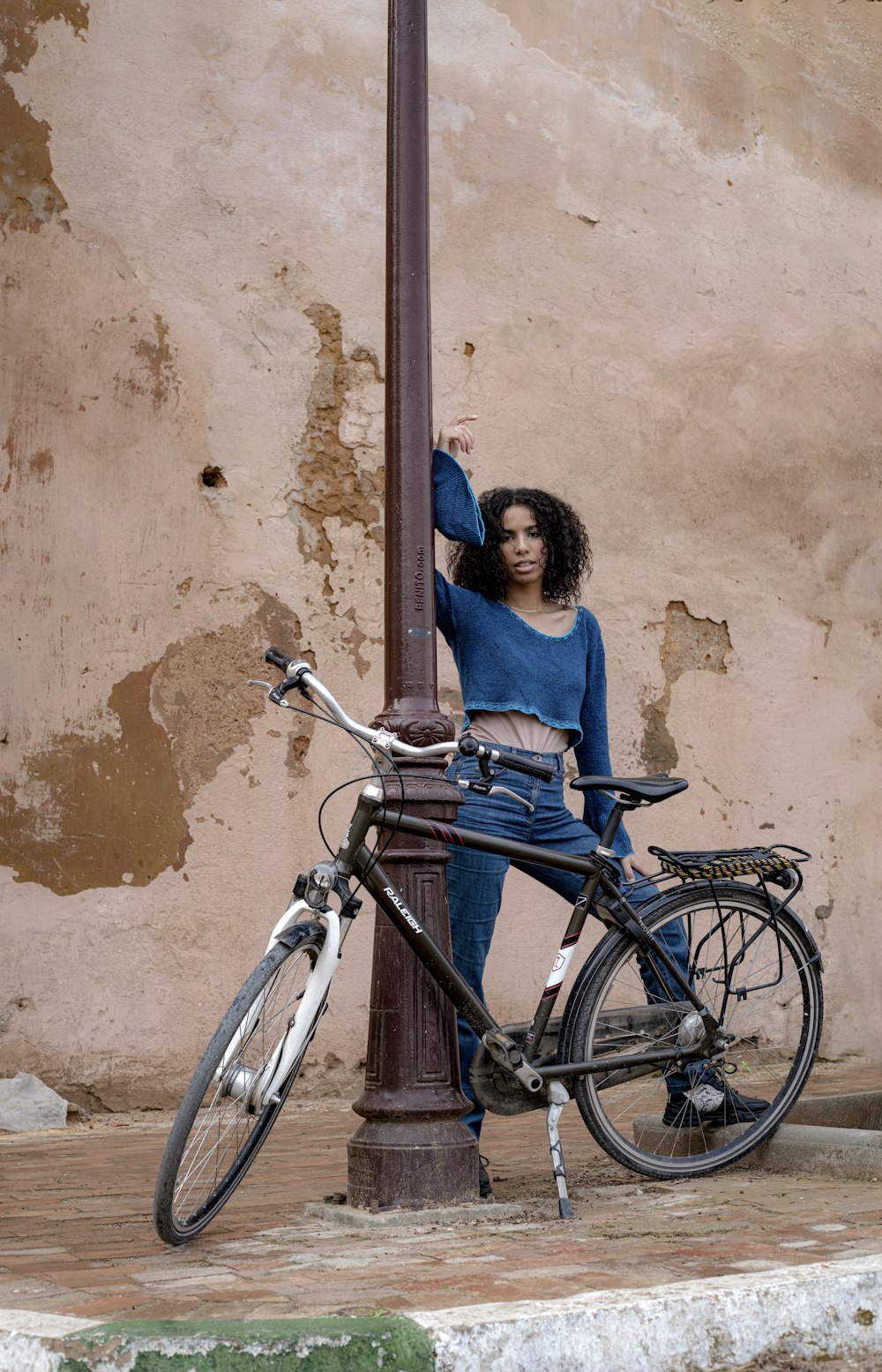 a woman leaning on a lamp post next to a bike