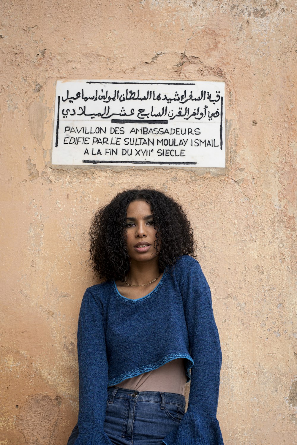 a woman leaning against a wall with a sign above her