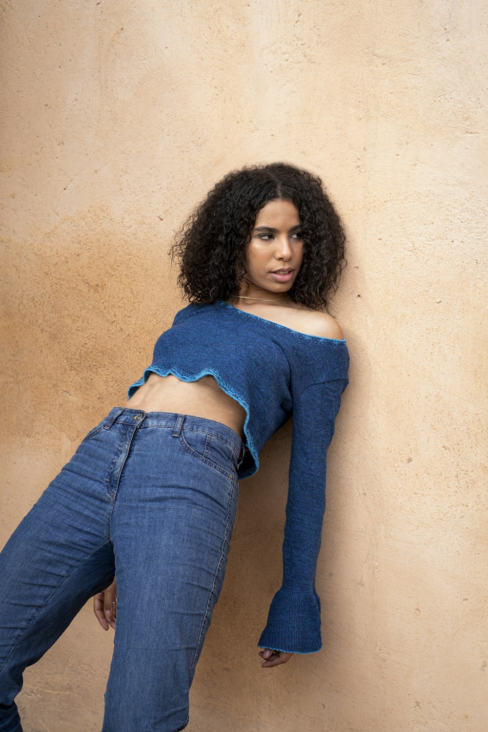 a woman leaning against a wall wearing a blue top