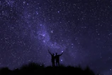A silhouette of two figures reaching out to each other beneath a starry sky filled with swirling constellations.