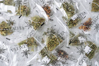 Multiple small transparent bags filled with dried herbal tea labeled 'CrystalTea High Quality CBD'. The bags display a leaf logo, and the herbs inside vary in color with some green and brown hues visible.