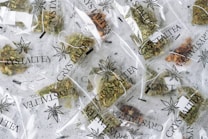 Multiple small transparent bags filled with dried herbal tea labeled 'CrystalTea High Quality CBD'. The bags display a leaf logo, and the herbs inside vary in color with some green and brown hues visible.
