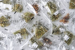 Multiple small transparent bags filled with dried herbal tea labeled 'CrystalTea High Quality CBD'. The bags display a leaf logo, and the herbs inside vary in color with some green and brown hues visible.
