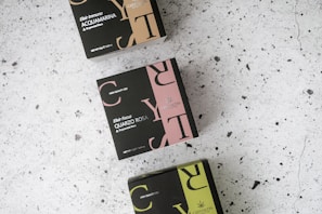 Three boxes with elegant, modern designs arranged on a speckled, light-colored surface. The boxes feature bold typography in colors such as beige, pink, and green, with text indicating different varieties of tea blends, including Acquamarina and Quarzo Rosa. Each box is labeled with 'High Quality CBD' and shows details like net weight.