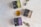 Three square boxes labeled with herbal tea names lie on a light textured surface. A glass cup filled with tea, containing a tea bag, is placed near the center. Two eucalyptus branches extend into the scene from the edges.